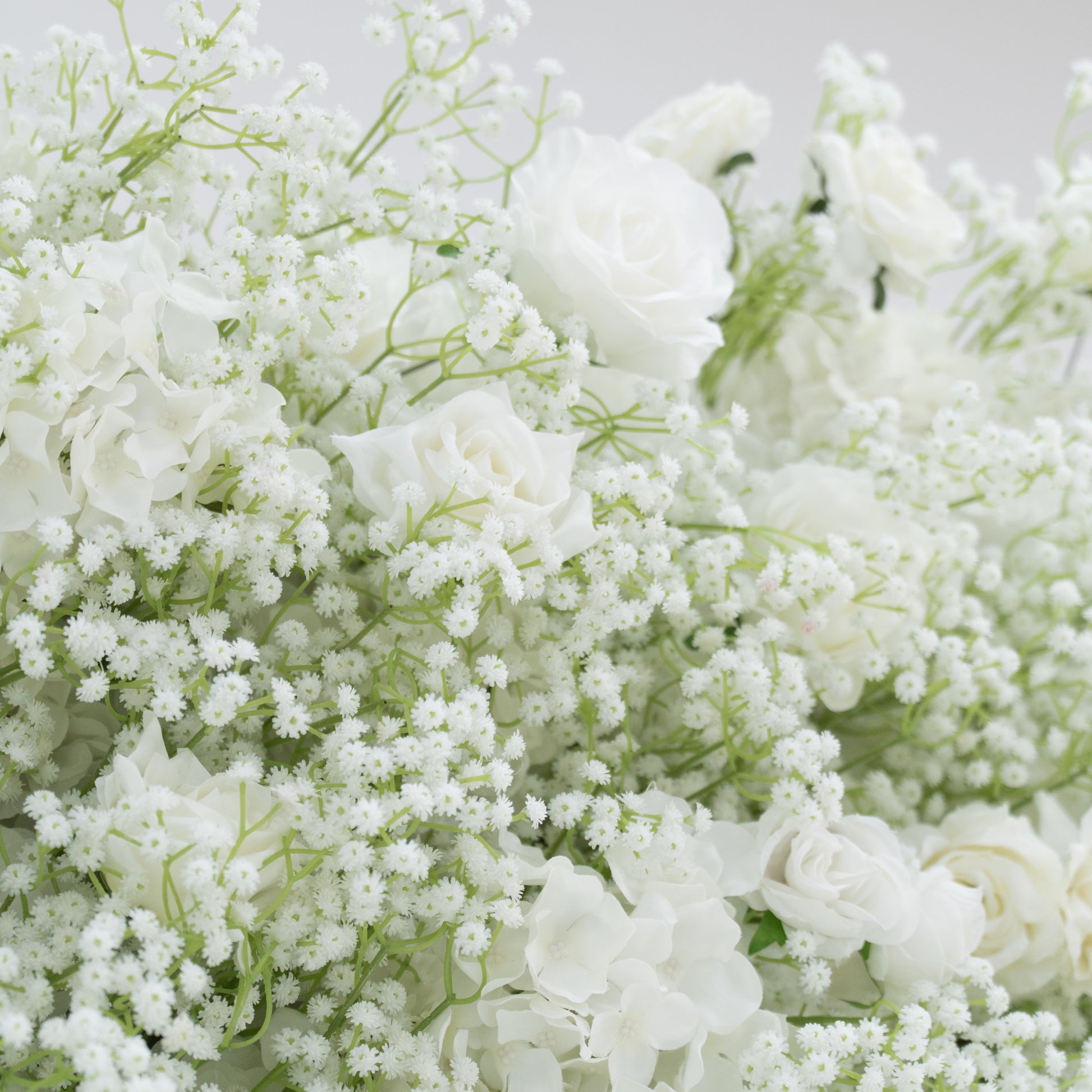 This image presents a lush arrangement of white flowers, including roses, hydrangeas, and baby's breath. The blooms are densely clustered, creating a soft, elegant, and pure visual effect. Set against a plain white background, the flowers exude a sense of tranquility and beauty, perfect for decorative purposes in events or as a symbol of innocence and grace.