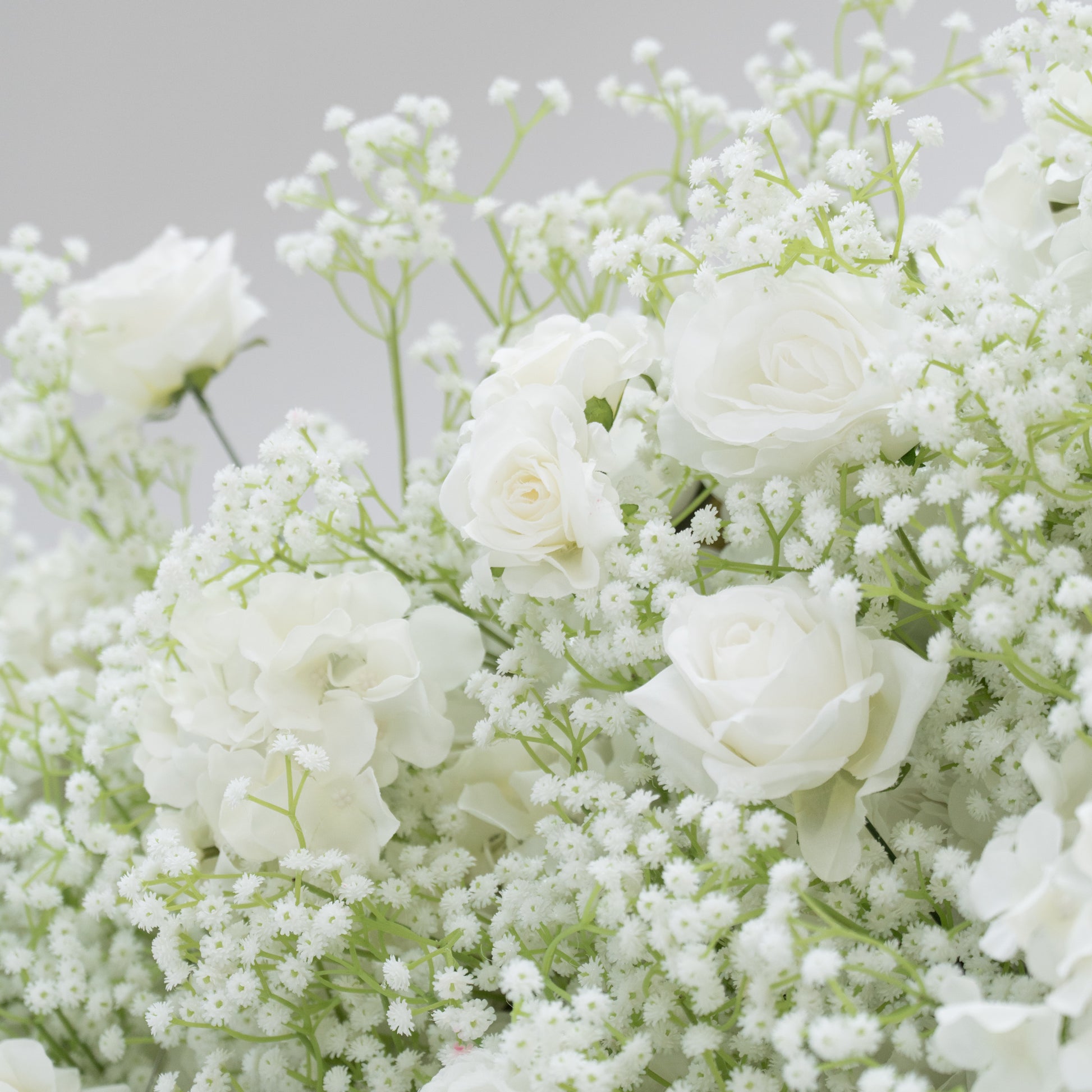This image showcases a lush arrangement of white flowers, including roses, hydrangeas, and baby's breath. The blooms are densely clustered, creating a soft, elegant, and pure visual effect. Set against a plain light - colored background, the flowers exude a sense of tranquility and beauty, perfect for decorative purposes in events or as a symbol of innocence and grace.
