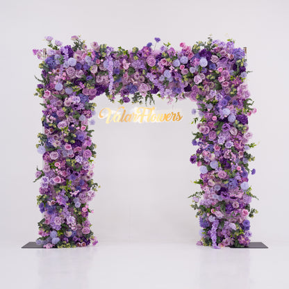 This image showcases a stunning floral arch by Valar Flowers, set against a plain white indoor background. It features a dense arrangement of artificial flowers in various shades of purple, lavender, and pink, creating an elegant, nature-inspired display. The brand’s name is elegantly integrated in gold, making it perfect for adding a luxurious, sophisticated element to events or interiors, highlighting Valar Flowers’ craftsmanship in eye-catching decor.