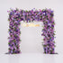 This image showcases a stunning floral arch by Valar Flowers, set against a plain white indoor background. It features a dense arrangement of artificial flowers in various shades of purple, lavender, and pink, creating an elegant, nature-inspired display. The brand’s name is elegantly integrated in gold, making it perfect for adding a luxurious, sophisticated element to events or interiors, highlighting Valar Flowers’ craftsmanship in eye-catching decor.