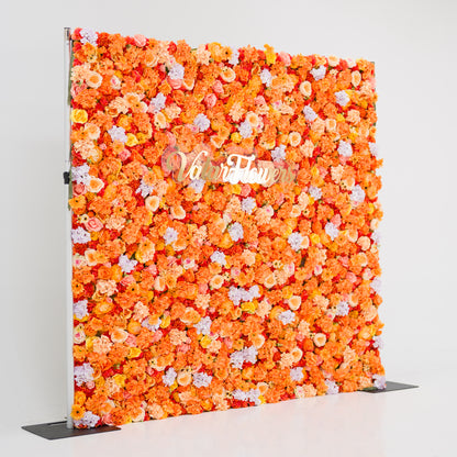 This image showcases a vibrant floral backdrop by Valar Flowers, featuring a dense arrangement of artificial flowers in warm shades of orange, peach, and hints of pink and purple. The textured display exudes energy and warmth, with the brand’s name elegantly integrated in gold. Set against a plain white indoor background, it’s perfect for adding a bold, nature-inspired element to events or interiors, highlighting Valar Flowers’ craftsmanship in creating eye-catching, sophisticated decor.