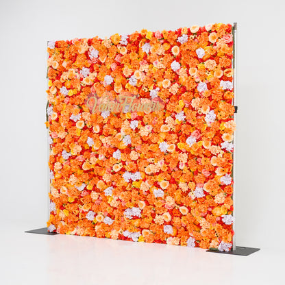This image showcases a vibrant floral backdrop by Valar Flowers, featuring a dense arrangement of artificial flowers in warm shades of orange, peach, and hints of pink and purple. The textured display exudes energy, with the brand’s name elegantly integrated in gold. Set against a plain white indoor background, it’s perfect for adding a bold, nature-inspired element to events or interiors.