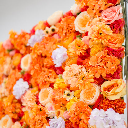 This image showcases a vibrant floral backdrop by Valar Flowers, featuring a dense arrangement of artificial flowers in warm shades of orange, peach, red, and hints of purple. The textured display, with varied blooms like roses and daisies, exudes energy and warmth. Perfect for adding a bold, nature-inspired element to events or interiors, it highlights the brand’s craftsmanship in creating eye-catching, sophisticated decor.