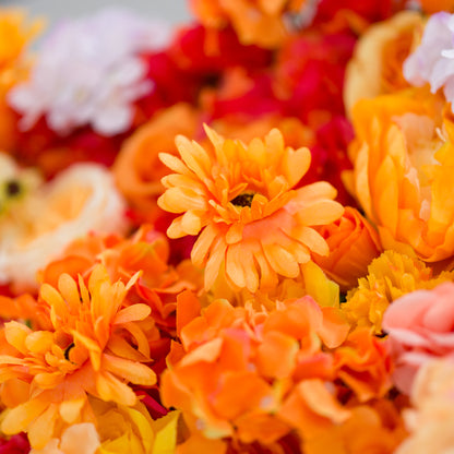This image showcases a vibrant section of a floral backdrop by Valar Flowers, featuring a dense arrangement of artificial flowers in warm shades of orange, peach, red, and hints of pink and purple. The textured display, with varied blooms like daisies and roses, exudes energy and warmth. Perfect for adding a bold, nature-inspired element to events or interiors, it highlights the brand’s craftsmanship in creating eye-catching, sophisticated decor.