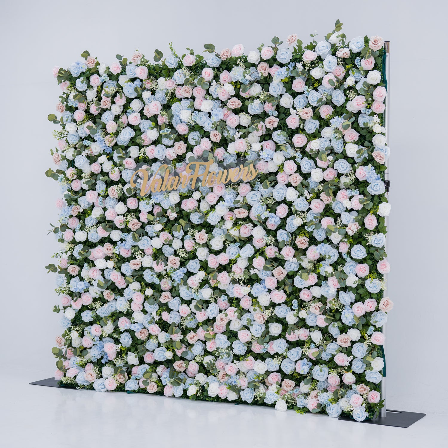This image showcases a vibrant floral backdrop by Valar Flowers, set against a plain white indoor background. It features a dense arrangement of artificial flowers in various shades of blue, light blue, and pink, with the brand’s name elegantly integrated in gold. Exuding elegance, it’s perfect for adding a sophisticated, nature-inspired element to events or interiors, highlighting Valar Flowers’ craftsmanship in detailed, eye-catching decor.