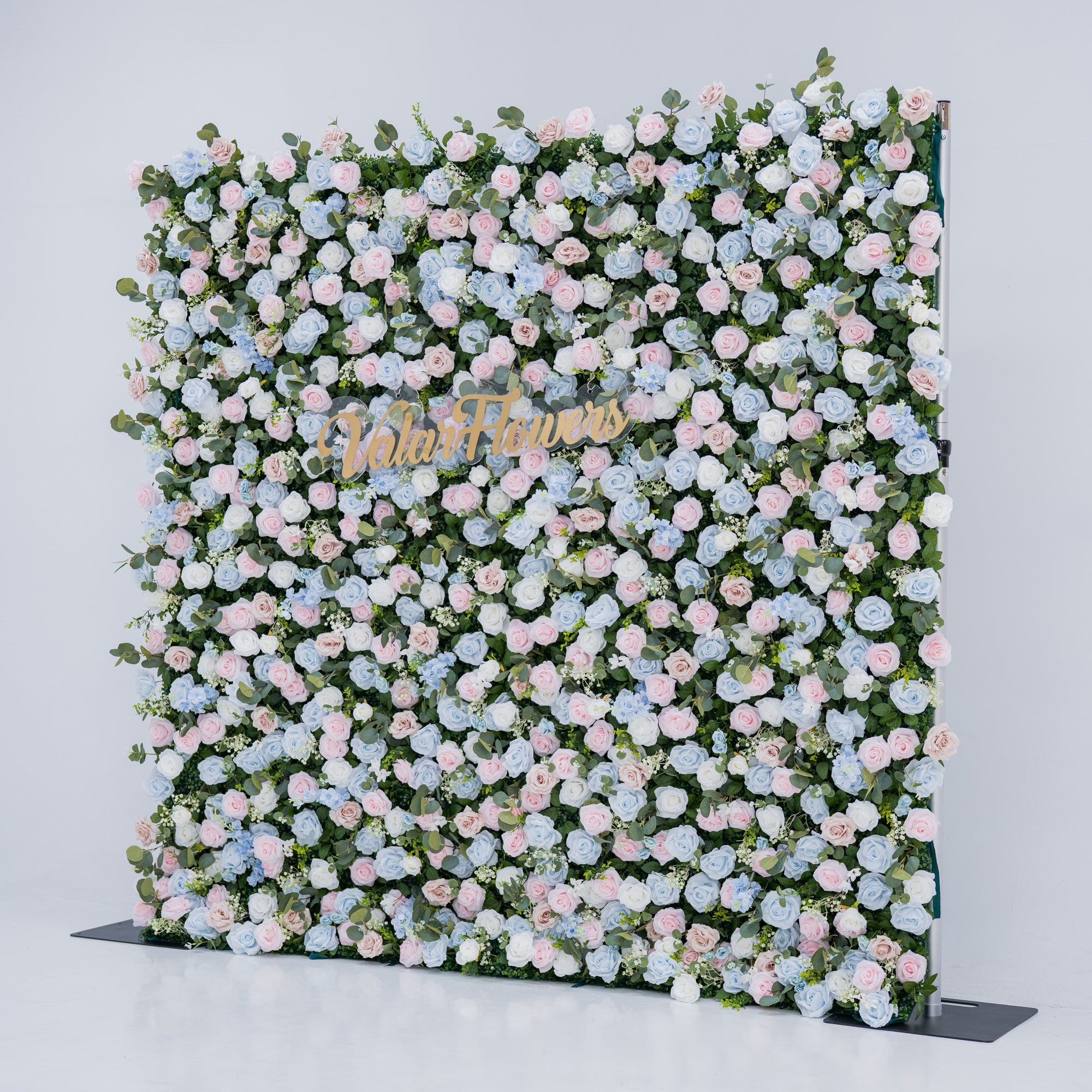 This image showcases a vibrant floral backdrop by Valar Flowers, set against a plain white indoor background. It features a dense arrangement of artificial flowers in various shades of blue, light blue, and pink, with the brand’s name elegantly integrated in gold. Exuding elegance, it’s perfect for adding a sophisticated, nature-inspired element to events or interiors, highlighting Valar Flowers’ craftsmanship in detailed, eye-catching decor.
