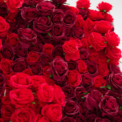 This lush close-up is a dense cascade of red roses, blending vivid crimson and deep burgundy hues. Their soft, ruffled petals create a velvety, romantic texture, filling the frame with rich, warm depth. The layered blooms exude passion and elegance, making this display ideal for romantic event decor, wedding styling, or intimate floral accents.
