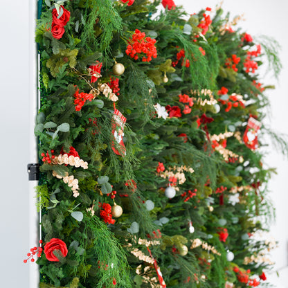 This sprawling festive backdrop (against a plain white background) is dense with lush green foliage (pine, feathery fronds), bold red roses, clustered blooms, and red berries. Accents include mini Santa stockings, gold/silver ornaments, and delicate gold sprays, arranged in repeating, lush patterns. A metallic frame edge peeks through, grounding the vibrant design. The rich red-and-green palette evokes cozy holiday charm—ideal for seasonal event decor or Christmas-themed backdrops.