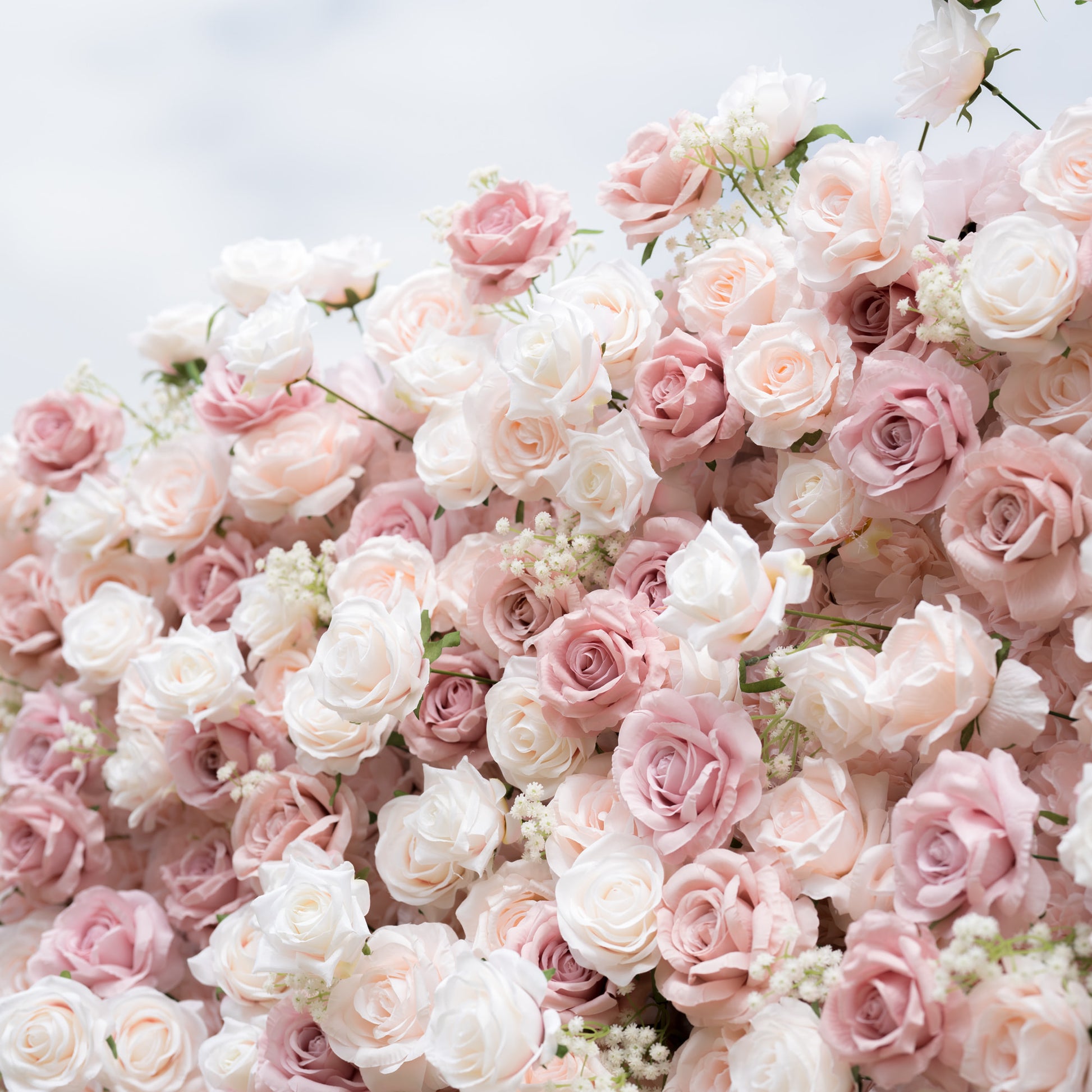 A close-up of a Valar Flowers floral arrangement, showcasing a lush, romantic blend of creamy white, soft blush, and dusty pink roses, interspersed with delicate baby's breath. The layered, textured blooms create a dreamy, elegant aesthetic, ideal for wedding backdrops and romantic event decor.