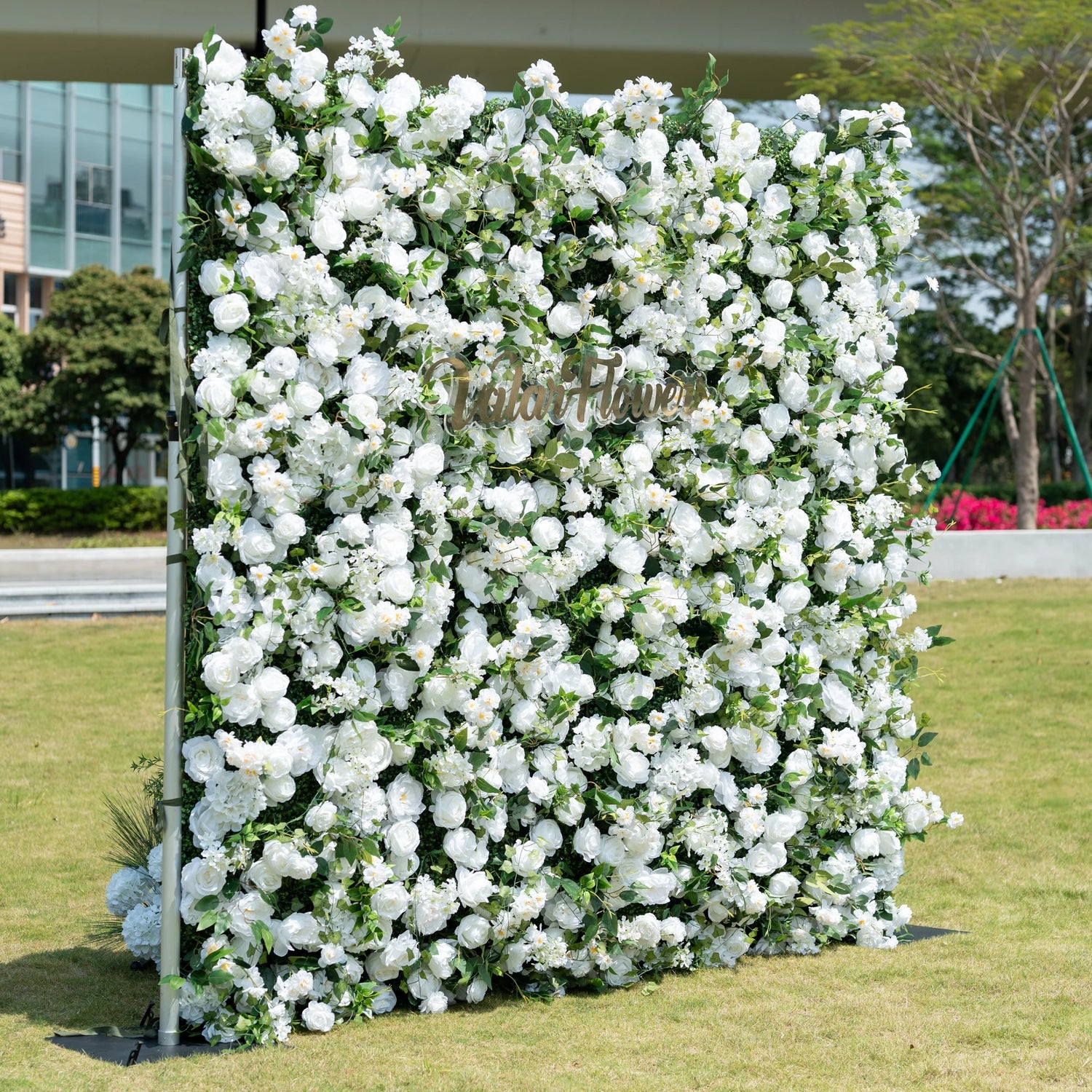 This is a premium all-white artificial flower wall backdrop by Valar Flowers, featuring a lush, dense design of soft roses, peonies, delicate baby’s breath, and subtle green foliage. Centered with the metallic "ValarFlowers" logo, this reusable, maintenance-free display creates an elegant, timeless focal point. Ideal for outdoor weddings, photo booths, luxury events, and brand activations, it offers a clean, romantic aesthetic perfect for professional styling.