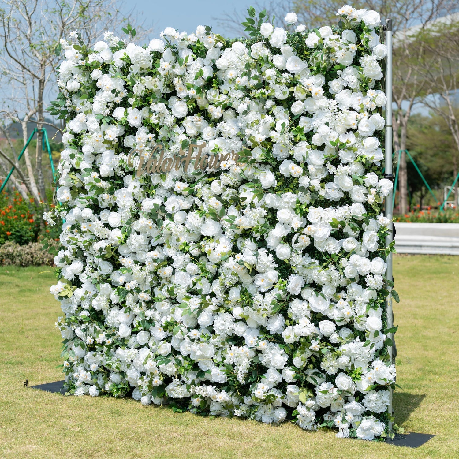 This is a premium all-white artificial flower wall backdrop by Valar Flowers, featuring a lush, dense design of soft roses, peonies, delicate baby’s breath, and subtle green foliage. Centered with the metallic "ValarFlowers" logo, this reusable, maintenance-free display creates an elegant, timeless focal point. Ideal for outdoor weddings, photo booths, luxury events, and brand activations, it offers a clean, romantic aesthetic perfect for professional styling.