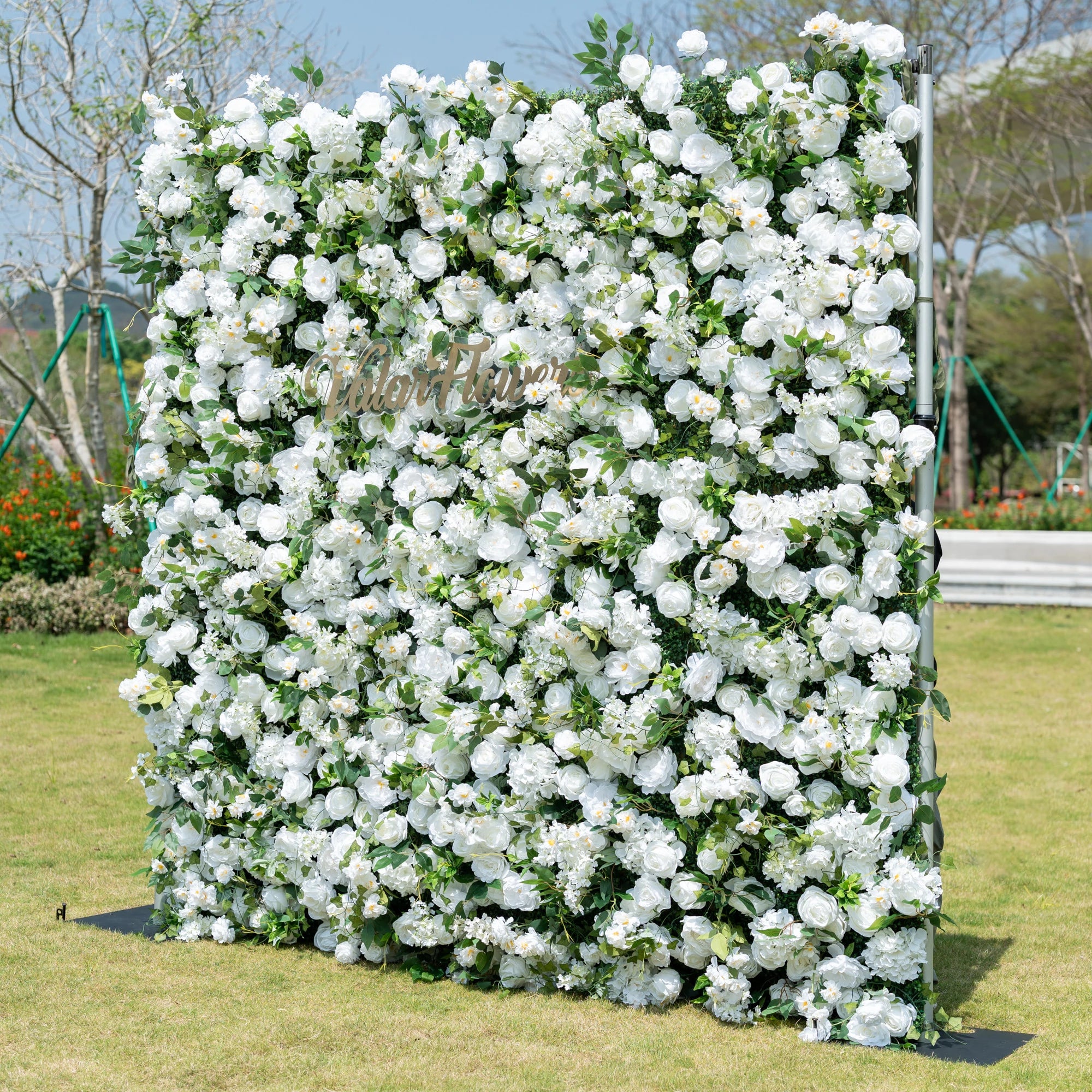 This is a premium all-white artificial flower wall backdrop by Valar Flowers, featuring a lush, dense design of soft roses, peonies, delicate baby’s breath, and subtle green foliage. Centered with the metallic "ValarFlowers" logo, this reusable, maintenance-free display creates an elegant, timeless focal point. Ideal for outdoor weddings, photo booths, luxury events, and brand activations, it offers a clean, romantic aesthetic perfect for professional styling.