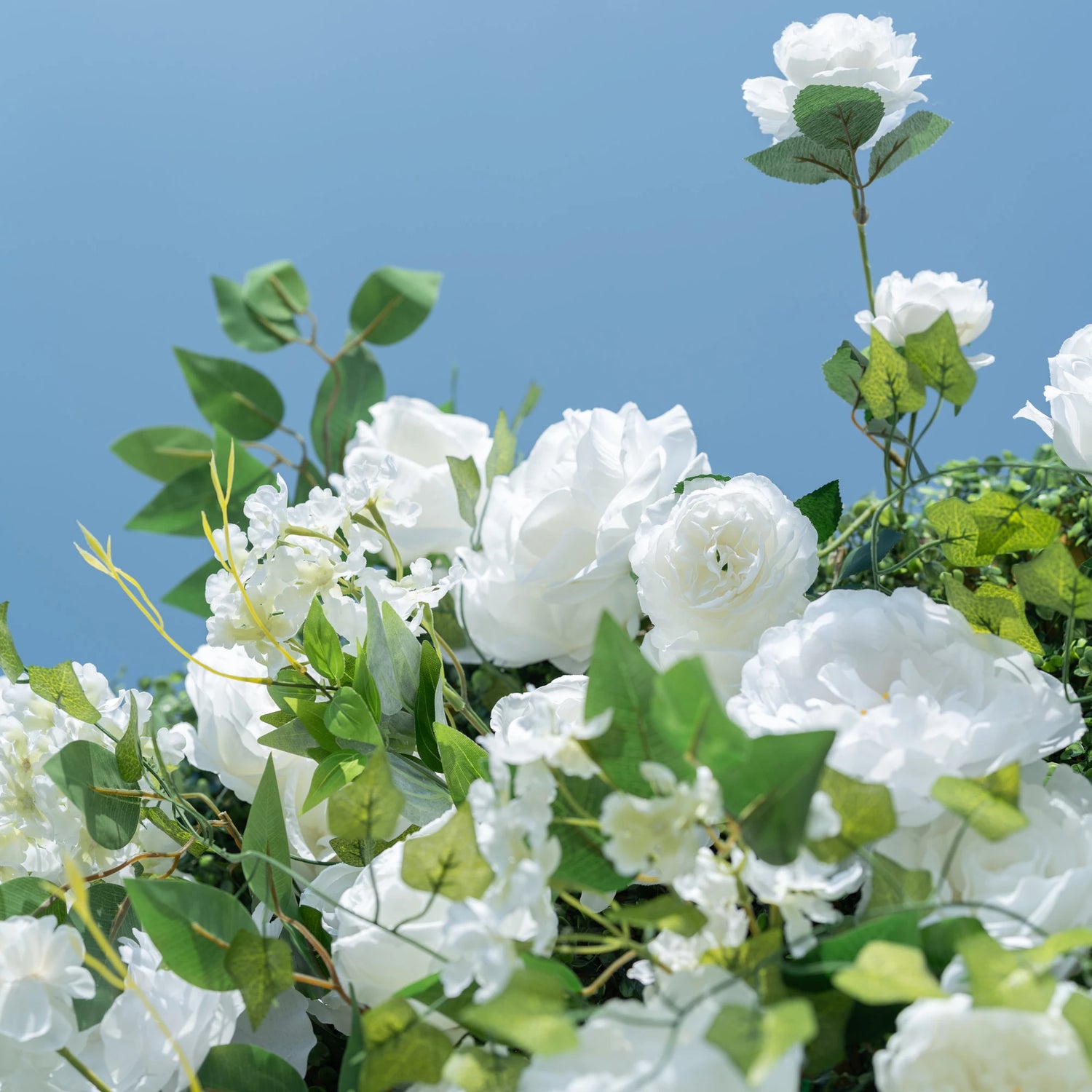 This close-up showcases Valar Flowers’ premium artificial floral design, featuring lush, hyper-realistic white roses, peonies, delicate filler blooms, and vibrant green foliage. Soft-textured petals mimic fresh flowers, while layered leaves and stems create a lifelike, maintenance-free display. Ideal for weddings, photo booths, and luxury events, this durable, reusable decor offers a clean, romantic aesthetic perfect for professional styling.