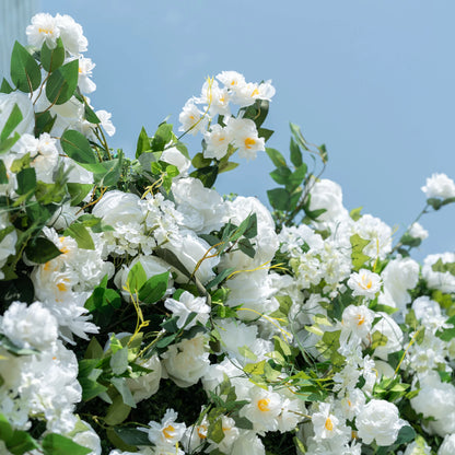 This close-up captures the lush top edge of Valar Flowers’ premium artificial white floral wall, set against a soft light blue sky. Featuring hyper-realistic roses, peonies, and delicate filler blooms paired with vibrant green foliage, the layered design creates a romantic, airy aesthetic. Soft-textured petals and lifelike leaves mimic fresh flowers, offering a maintenance-free, durable display ideal for weddings, photo booths, and luxury events.