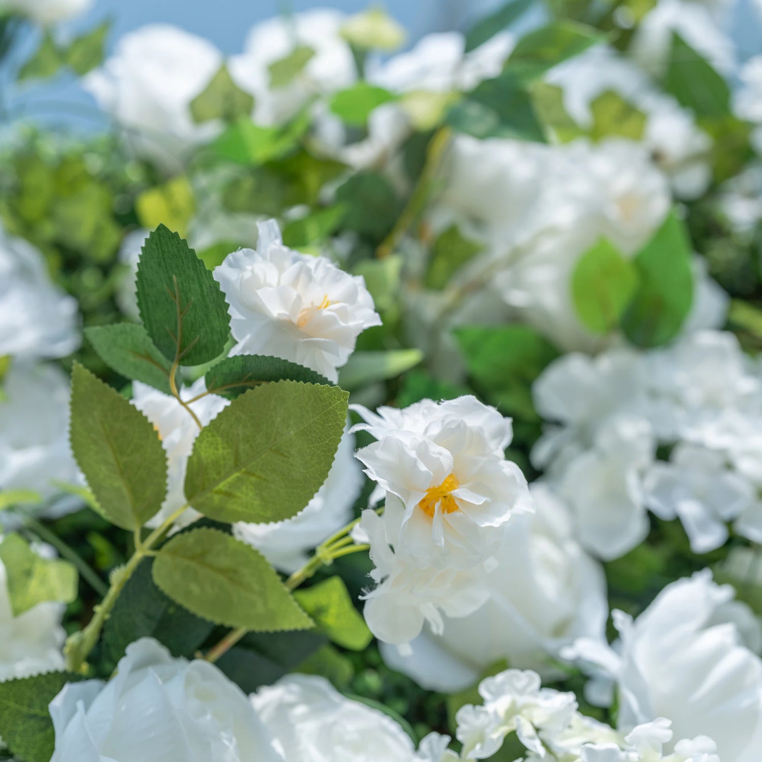 This close-up highlights Valar Flowers’ premium artificial white blooms, featuring delicate layered petals with soft yellow centers and hyper-realistic textured green foliage. The shallow depth of field emphasizes the intricate details of the flowers, creating a lifelike, romantic aesthetic. Maintenance-free and durable, these blooms are ideal for weddings, photo booths, and luxury events, offering a clean, timeless look perfect for professional styling.