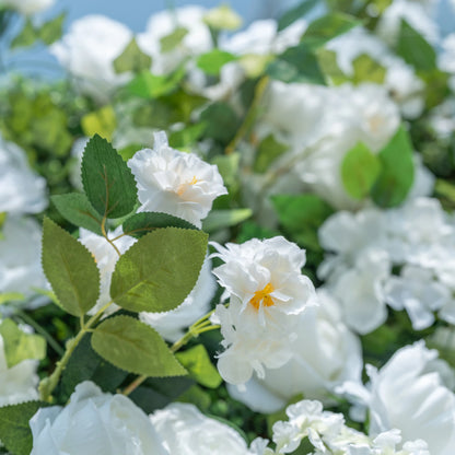 This close-up highlights Valar Flowers’ premium artificial white blooms, featuring delicate layered petals with soft yellow centers and hyper-realistic textured green foliage. The shallow depth of field emphasizes the intricate details of the flowers, creating a lifelike, romantic aesthetic. Maintenance-free and durable, these blooms are ideal for weddings, photo booths, and luxury events, offering a clean, timeless look perfect for professional styling.