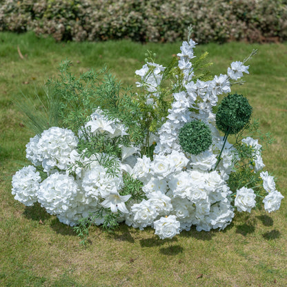 This premium artificial floral arrangement by Valar Flowers features a lush mix of white roses, hydrangeas, lilies, delphiniums, and textured green foliage. Designed for weddings, photo booths, and luxury events, this dense, realistic display offers a clean, timeless aesthetic. Maintenance-free and durable, it brings a romantic, elegant touch to any setting, perfect for professional styling and event decor.