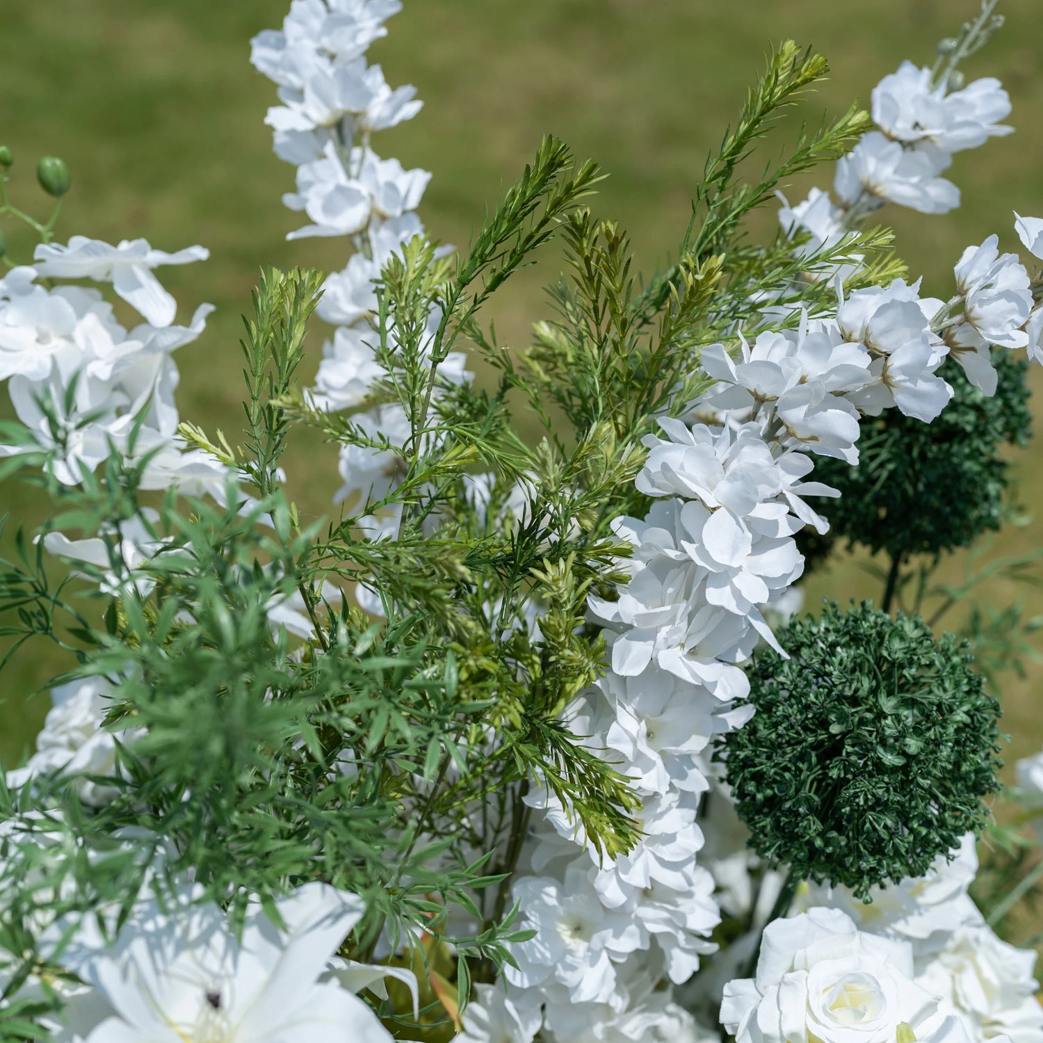 This close-up captures Valar Flowers’ premium artificial floral arrangement, featuring delicate white delphinium blooms, feathery green foliage, and spherical green accents. The layered design creates depth, with lifelike petals and textured greenery mimicking fresh flowers. Maintenance-free and durable, this elegant display is ideal for weddings, photo booths, and luxury events, offering a clean, romantic aesthetic perfect for professional styling.