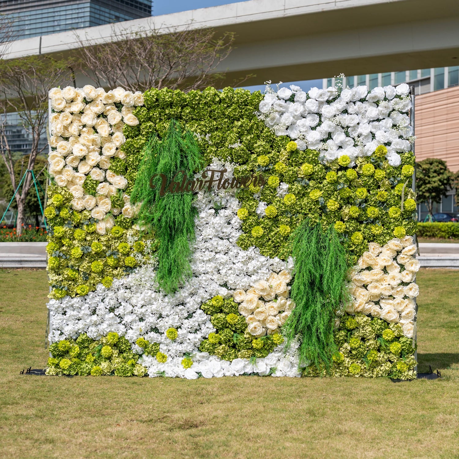 This is a premium green and white artificial flower wall backdrop by Valar Flowers, featuring a lush nature-inspired design with vibrant green hydrangeas, ivory roses, crisp white blooms, and cascading foliage. The custom "ValarFlowers" logo sign adds a personalized touch. This reusable, maintenance-free floral display creates a fresh, elegant focal point, ideal for outdoor weddings, garden parties, photo booths, and luxury events, offering long-lasting beauty for professional decor.