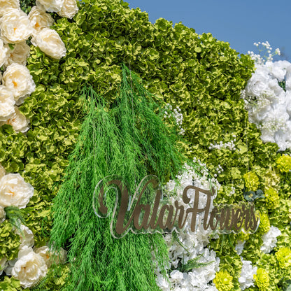 This close-up showcases Valar Flowers’ premium artificial flower wall, featuring lush, vibrant green hydrangeas, cascading foliage, soft white blooms, and ivory roses, complemented by a sleek metallic “ValarFlowers” logo sign. High-quality, hyper-realistic petals and dense, layered greenery create a lifelike, maintenance-free display, ideal for wedding backdrops, photo booths, and luxury events, offering a fresh, elegant aesthetic for professional decor.