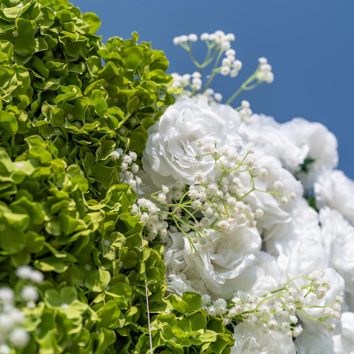 This close-up showcases Valar Flowers’ premium artificial floral wall, featuring lush, vibrant green hydrangeas, soft white roses, and delicate baby’s breath. The hyper-realistic petals and dense, layered foliage mimic fresh blooms, creating a lifelike, maintenance-free display. Ideal for wedding backdrops, photo booths, and luxury events, this durable, reusable decor offers a fresh, elegant aesthetic for professional styling.