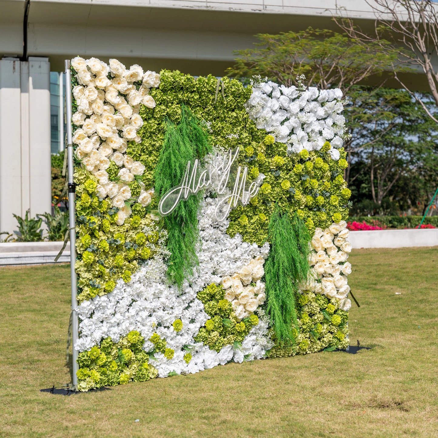 This is a stunning 10x8ft artificial flower wall backdrop by Valar Flowers, featuring a lush, nature-inspired design with vibrant green hydrangeas, cascading foliage, soft ivory roses, and crisp white blooms. Centered with a custom "Marry Me" neon sign, this reusable, maintenance-free display creates a romantic focal point, ideal for outdoor weddings, proposals, photo booths, and luxury events, offering long-lasting beauty for professional decor.