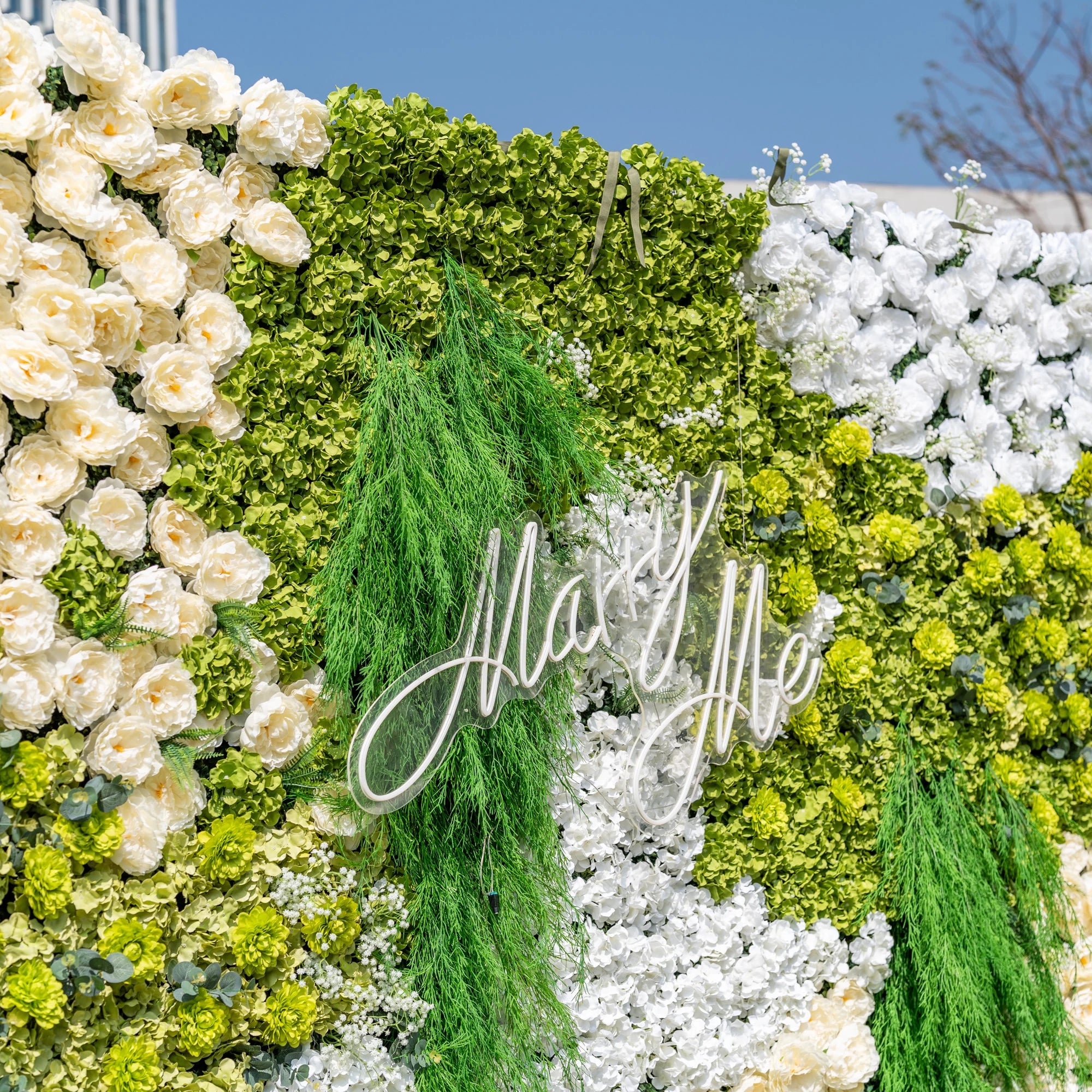 This close-up highlights Valar Flowers’ premium artificial floral wall, featuring lush green hydrangeas, cascading foliage, soft ivory roses, and crisp white blooms, with a glowing "Marry Me" neon sign. The hyper-realistic petals and dense, layered greenery create a romantic, maintenance-free display, ideal for proposals, weddings, photo booths, and luxury events, offering an elegant, nature-inspired aesthetic for professional decor.