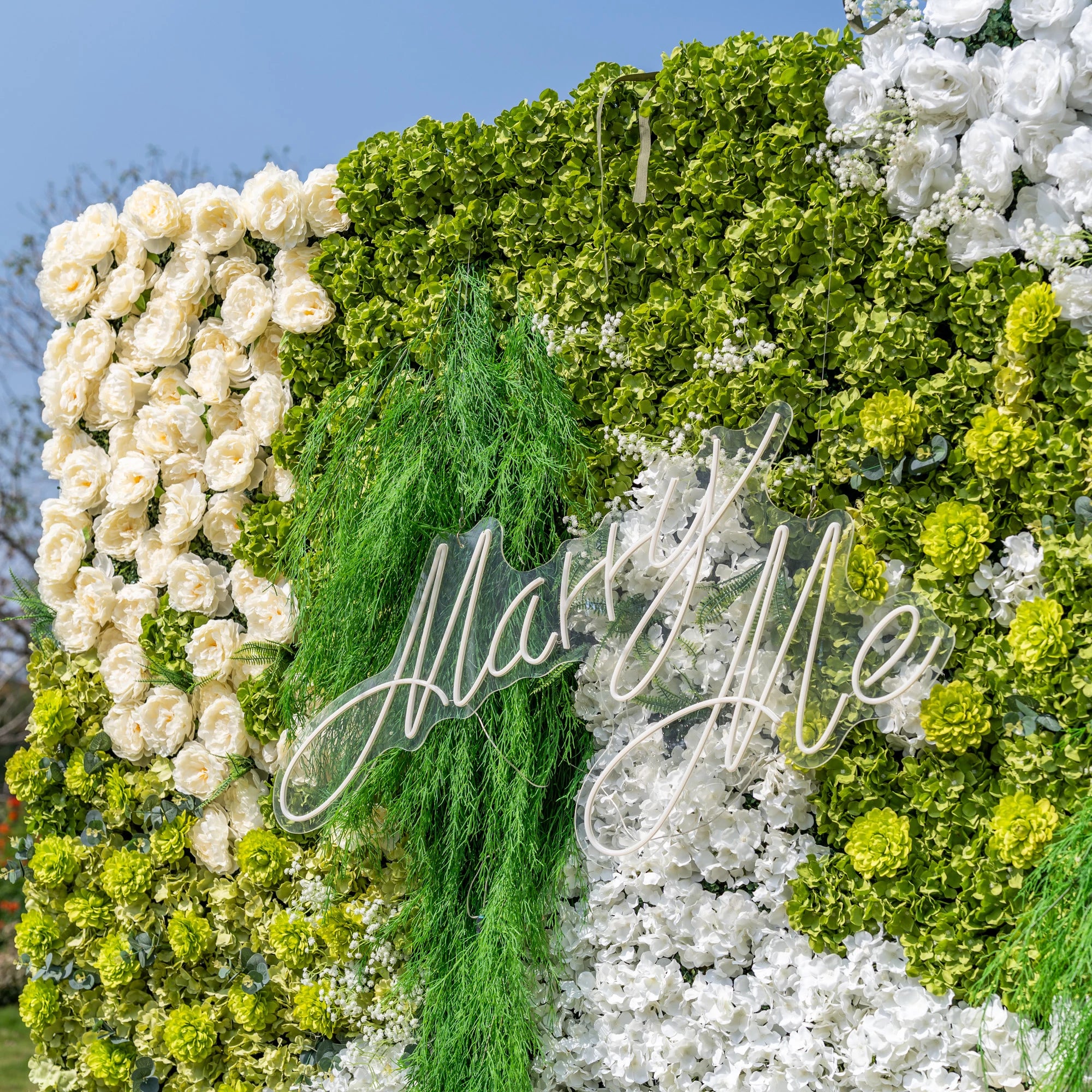 This close-up highlights Valar Flowers’ premium artificial floral wall, featuring lush green hydrangeas, cascading foliage, soft ivory roses, and crisp white blooms, with a glowing "Marry Me" neon sign as the centerpiece. The hyper-realistic petals and dense, layered greenery create a romantic, maintenance-free display. Ideal for proposals, weddings, photo booths, and luxury events, this decor offers an elegant, nature-inspired aesthetic perfect for special occasions.