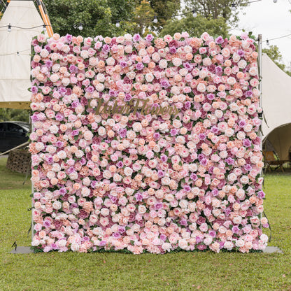 Three-quarter angle of Valar Flowers Sunset Romance artificial flower wall showcasing layered pink peach and lavender roses with ivory hydrangeas outdoors against white tents and string lights for enchanting garden wedding ceremonies and bridal showers