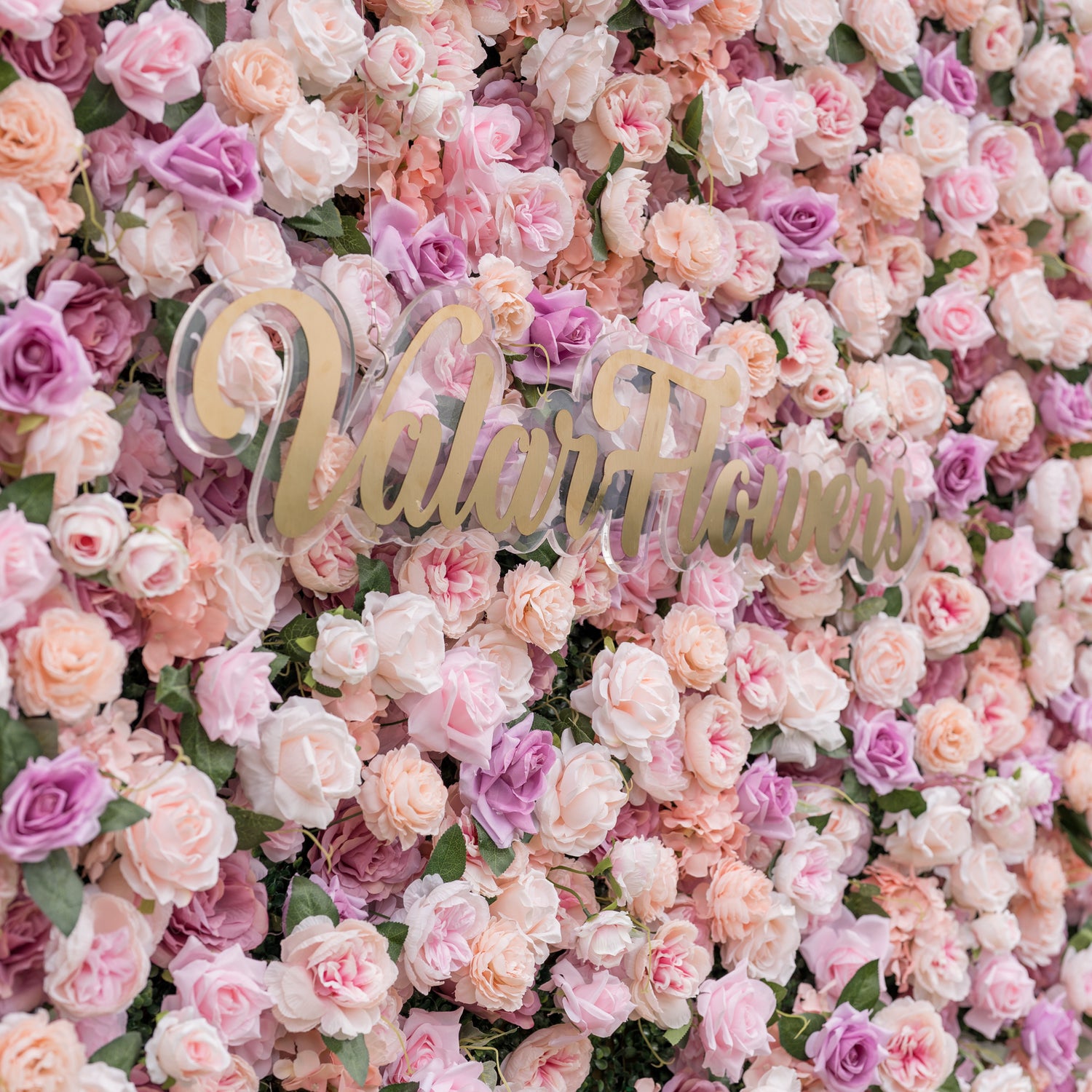 Low-angle close-up of Valar Flowers artificial flower wall emphasizing sculptural depth of blush roses peach peonies and ivory hydrangeas on fabric base with dreamy defocused garden background for romantic wedding ceremonies and sweetheart table backdrops