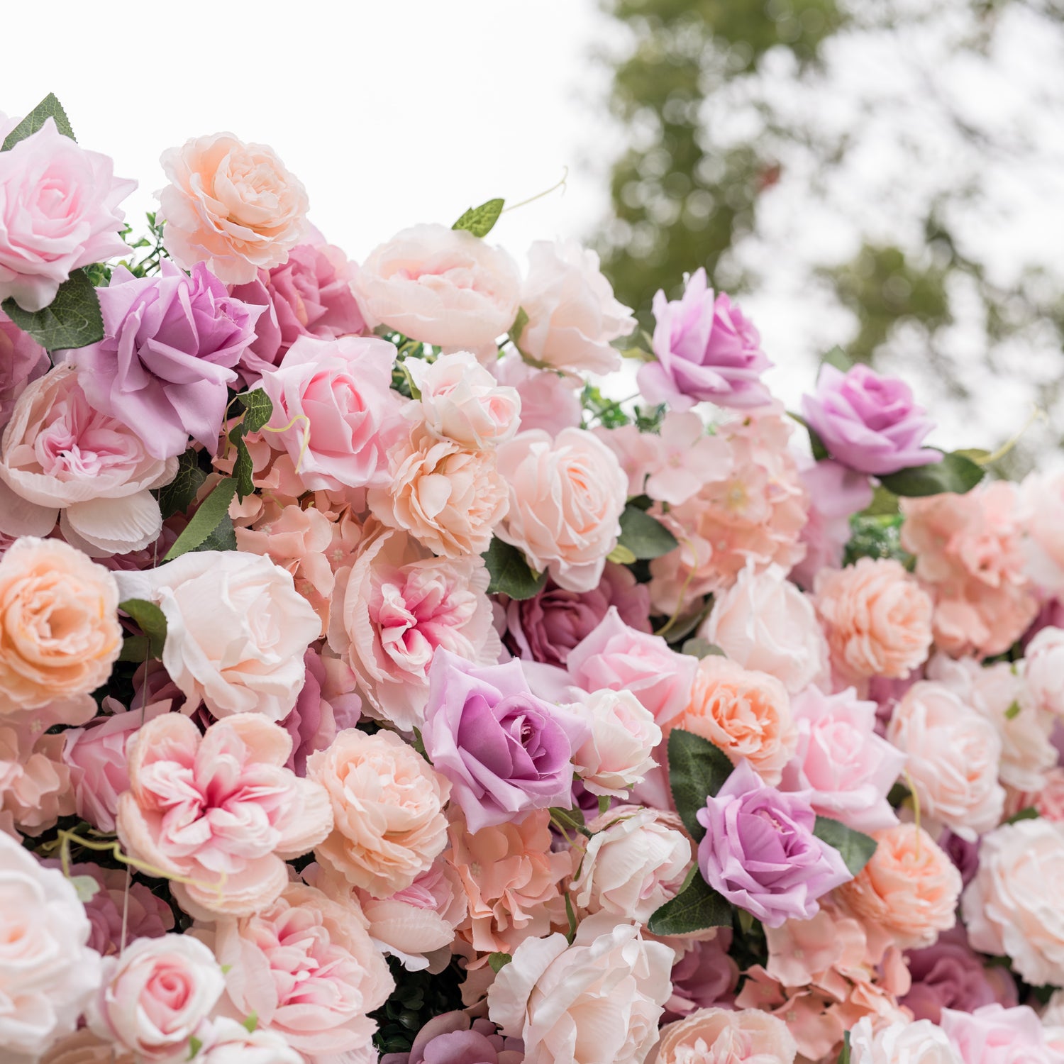 Angled close-up of Valar Flowers wall with gold cursive Valor Flowers sign nestled among blush pink and dusty rose blooms against soft outdoor greenery an elegant branded focal point for luxury weddings and upscale corporate event photo opportunities