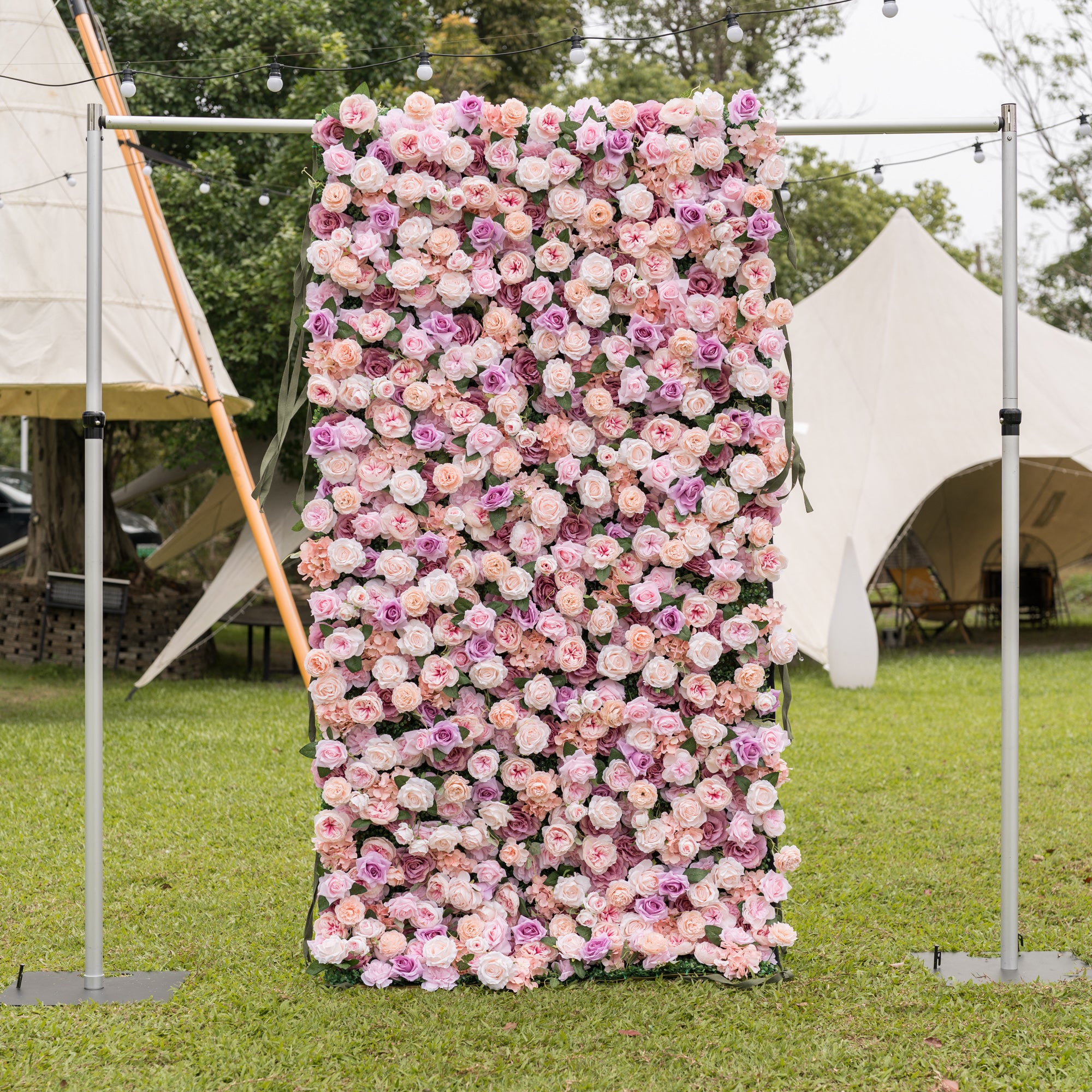 Frontal view of Valar Flowers Sunset Romance wall on silver metal frame with blush pink dusty rose peach and lavender roses peonies and hydrangeas on manicured lawn with teepee canopy behind for sophisticated outdoor receptions and luxury garden galas