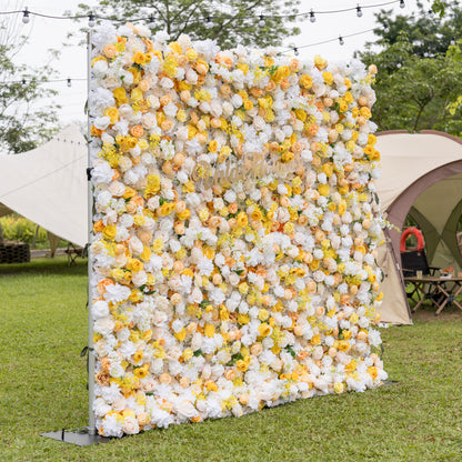 Three-quarter view of Valar Flowers rose hydrangea wall blending white yellow peach blooms with gold cursive sign, set outdoors with canvas tents and globe lights. Festive floral backdrop for garden celebrations and outdoor receptions.