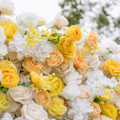 Low-angle close-up of Valar Flowers wall: voluminous cream roses, yellow ranunculus, peach blooms with dreamy defocused garden background. Airy romance for spring summer events and luxury bridal backdrops.