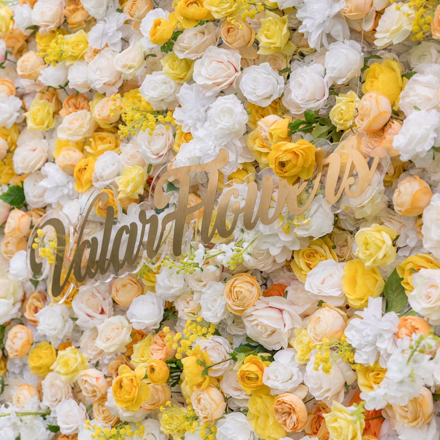 Angled close-up of Valar Flowers wall with gold cursive Valor Flowers sign among white yellow peach roses against soft outdoor greenery. Elegant branded focal point for corporate events and luxury wedding backdrops.