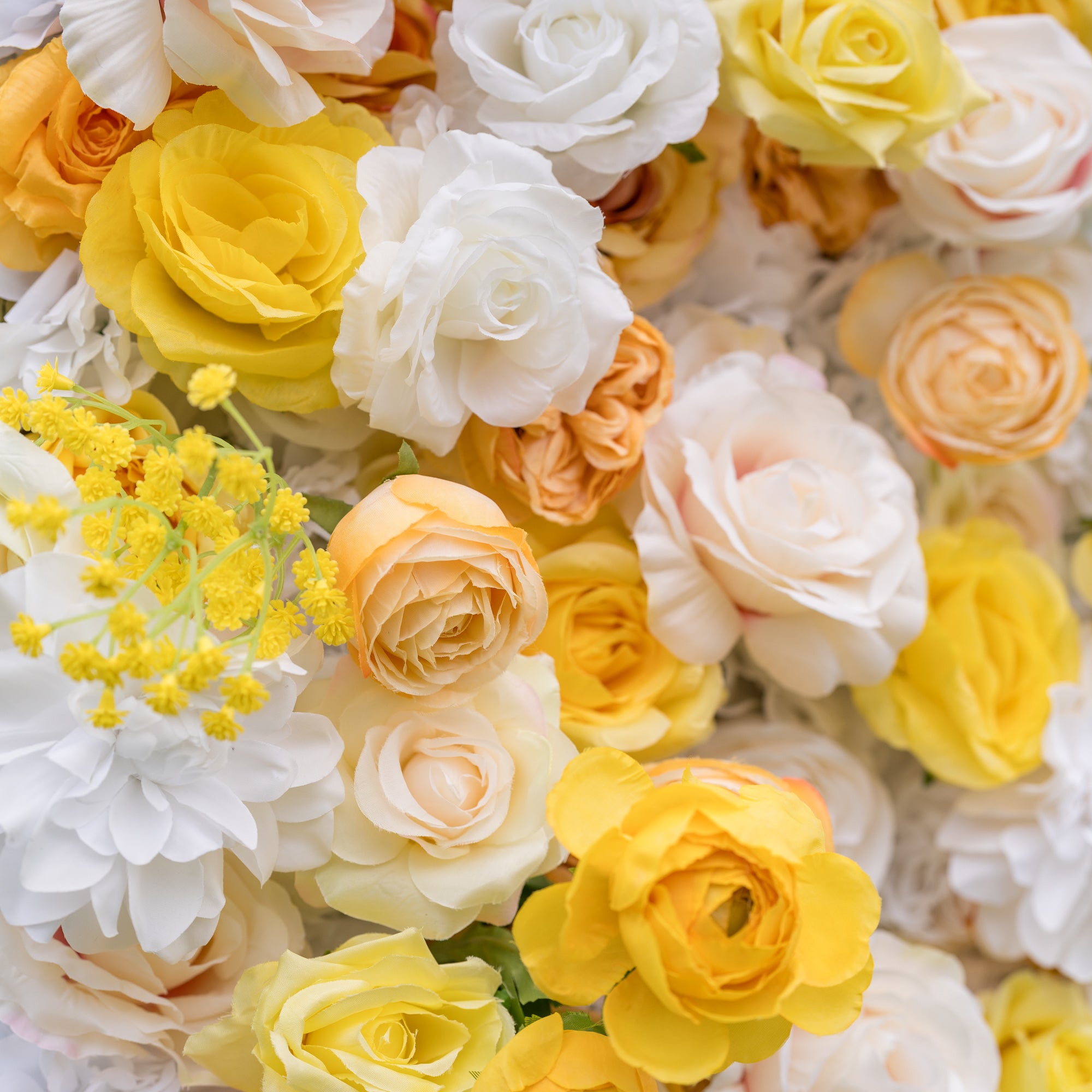 Elevated close-up of Valar Flowers wall: open roses and ranunculus in buttery yellow, lemon, white, and peach with bright filler sprays. Vibrant sunlit garden feel for spring celebrations and outdoor wedding photo booths.