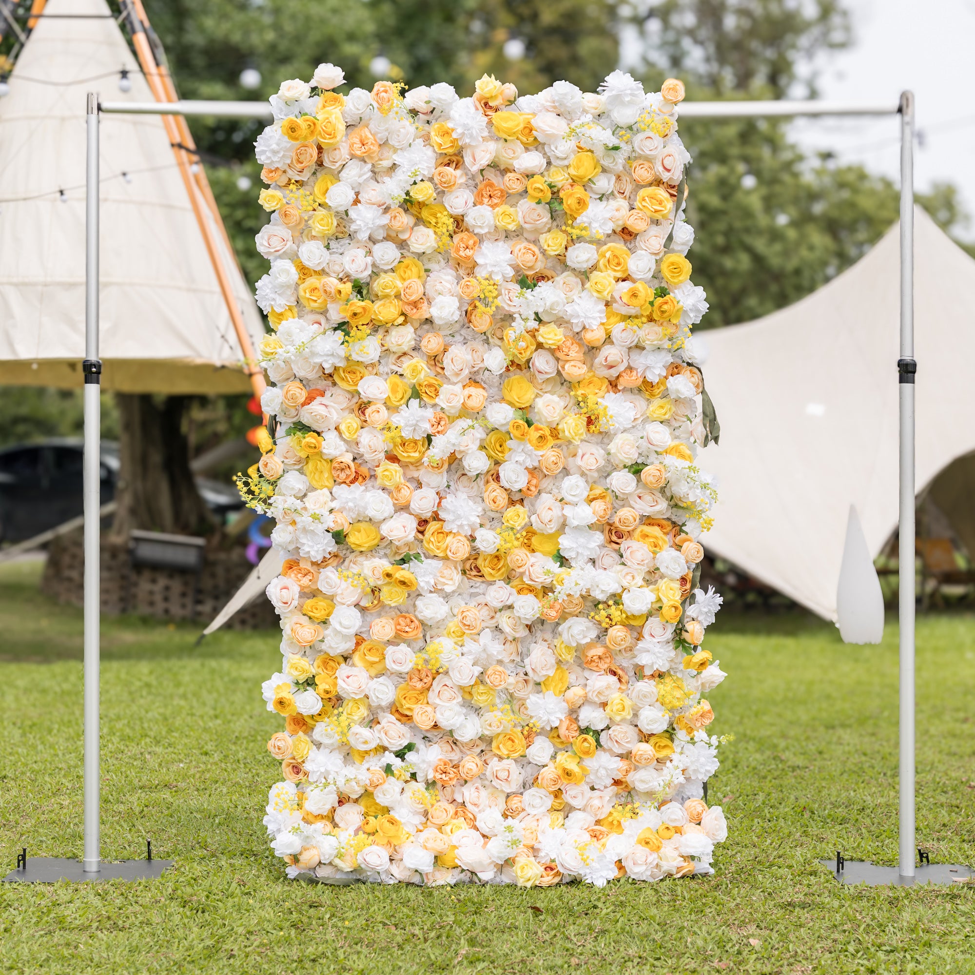 Frontal view of Valar Flowers wall on silver frame: white, buttery yellow, and peach roses on manicured lawn with teepee canopy blurred behind. Sophisticated elegance for outdoor wedding receptions and garden galas.