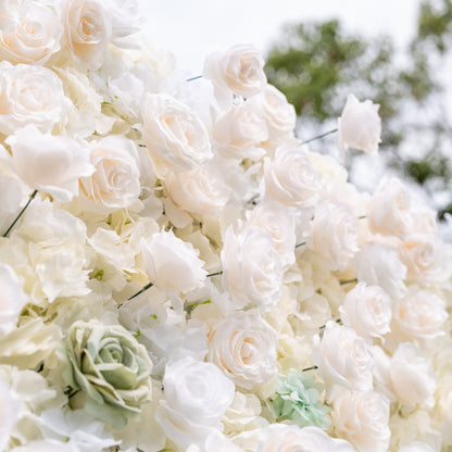Angled close-up of Valar Flowers wall with gold cursive Valor Flowers sign among dusty blue and sage green roses against soft outdoor greenery an elegant branded focal point for modern weddings and upscale corporate event photo opportunities