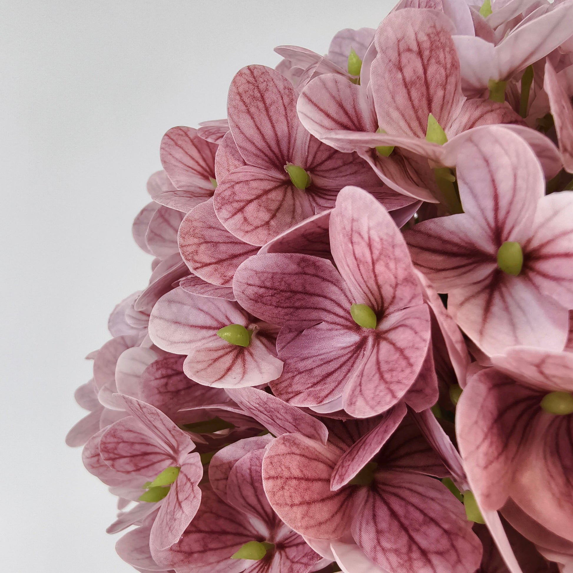 This is a close - up of artificial pink hydrangea flowers. The petals have delicate purple veins and green centers, creating a realistic texture. The clustered blooms form a lush, rounded shape, ideal for adding a soft, romantic touch to decor, with their pastel hue and intricate detailing. 