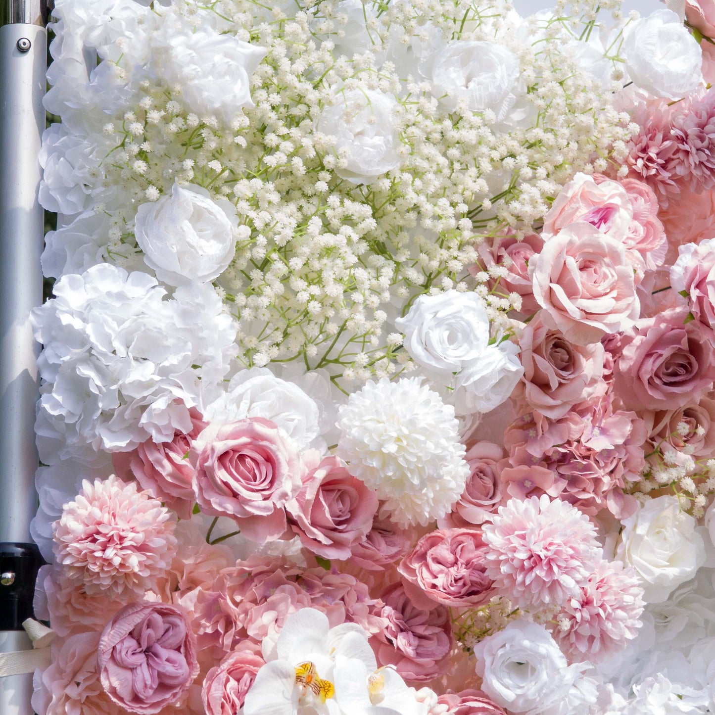 This backdrop features a lush arrangement of artificial flowers. Prominent flowers include white and pink roses, white hydrangeas, and clusters of baby's breath. The color palette consists of soft pinks, pure whites, and light green accents from the foliage. The style is romantic and delicate, ideal for creating a dreamy atmosphere at events like weddings. 