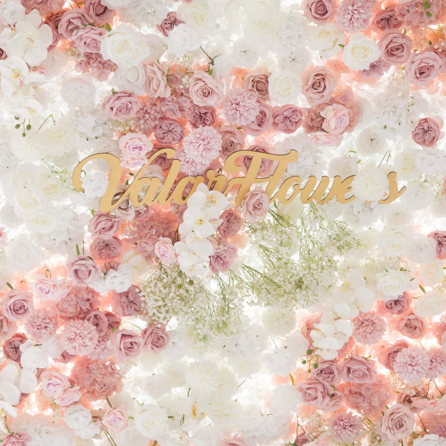 This backdrop is a lush floral wall composed of artificial flowers. It features roses in various shades of pink and white, white orchids, and clusters of baby's breath. The color palette is soft and pastel - toned, with gentle pinks, creams, and whites. The style is romantic and elegant, ideal for wedding or bridal events. The "ValarFlowers" sign in gold adds a touch of branding. 