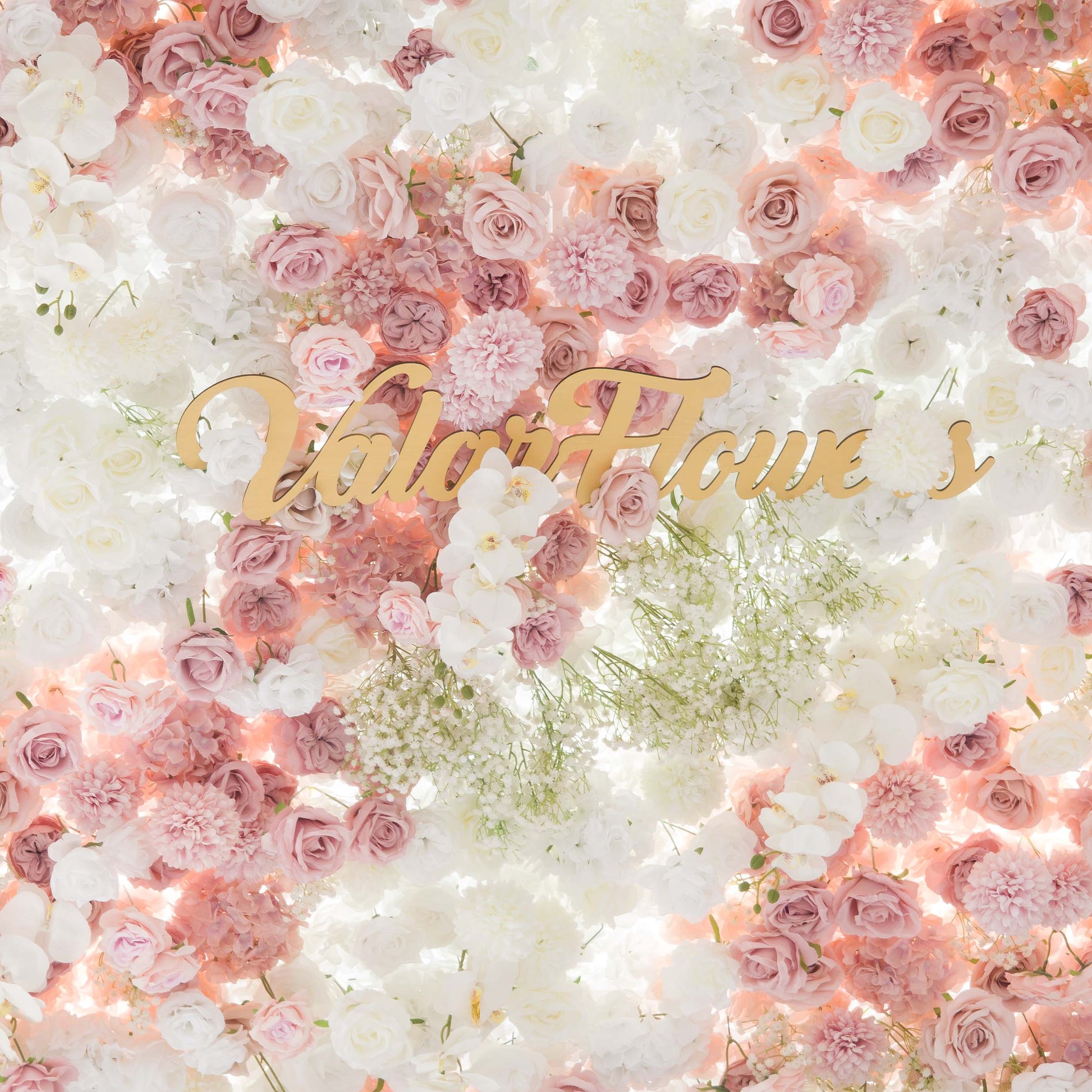 This backdrop is a lush floral wall composed of artificial flowers. It features roses in various shades of pink and white, white orchids, and clusters of baby's breath. The color palette is soft and pastel - toned, with gentle pinks, creams, and whites. The style is romantic and elegant, ideal for wedding or bridal events. The "ValarFlowers" sign in gold adds a touch of branding. 