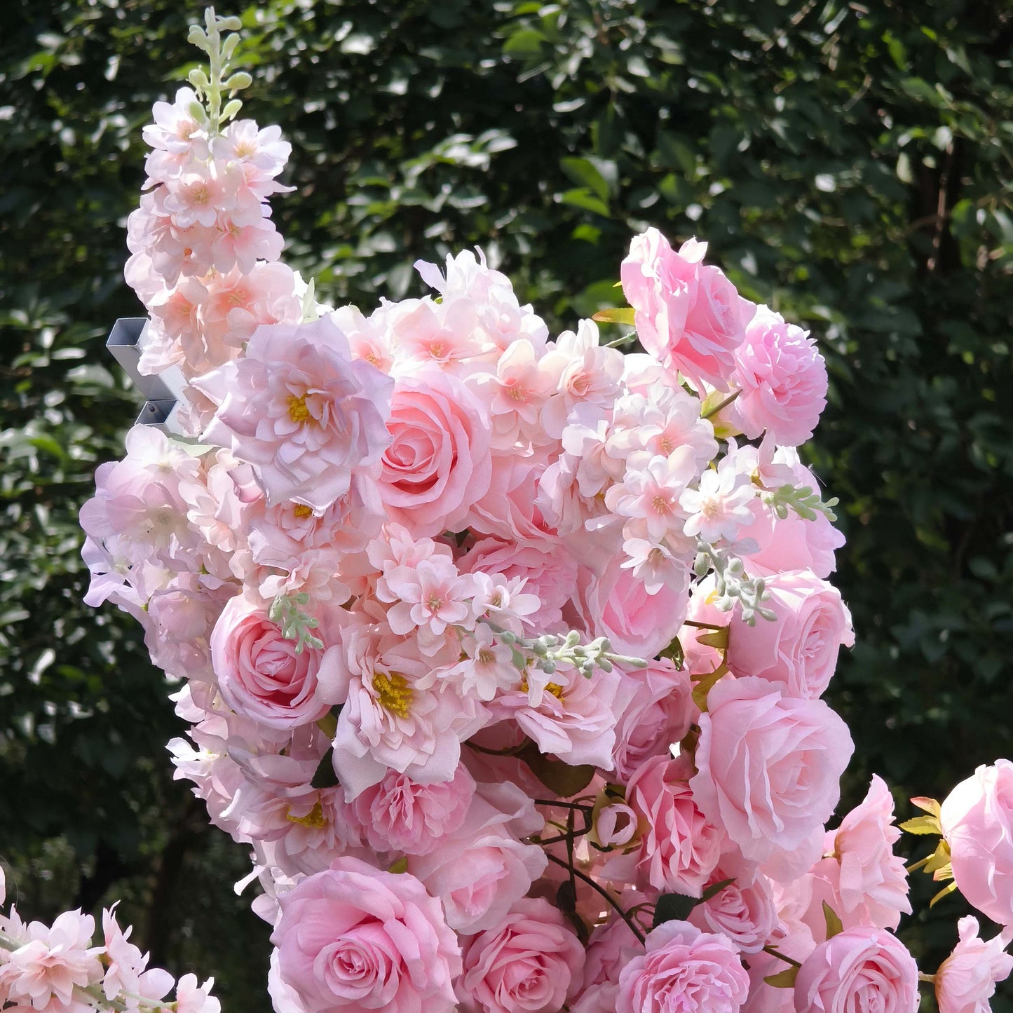 This close-up from Valar Flowers captures a lush, romantic cluster of soft pink blooms—including velvety roses, delicate peonies, and airy sprigs—arranged in a cascading, organic shape. Set against a backdrop of vibrant green foliage, the velvety petals and layered textures create a dreamy, fresh atmosphere, ideal for outdoor weddings, engagement shoots, or elegant celebrations.