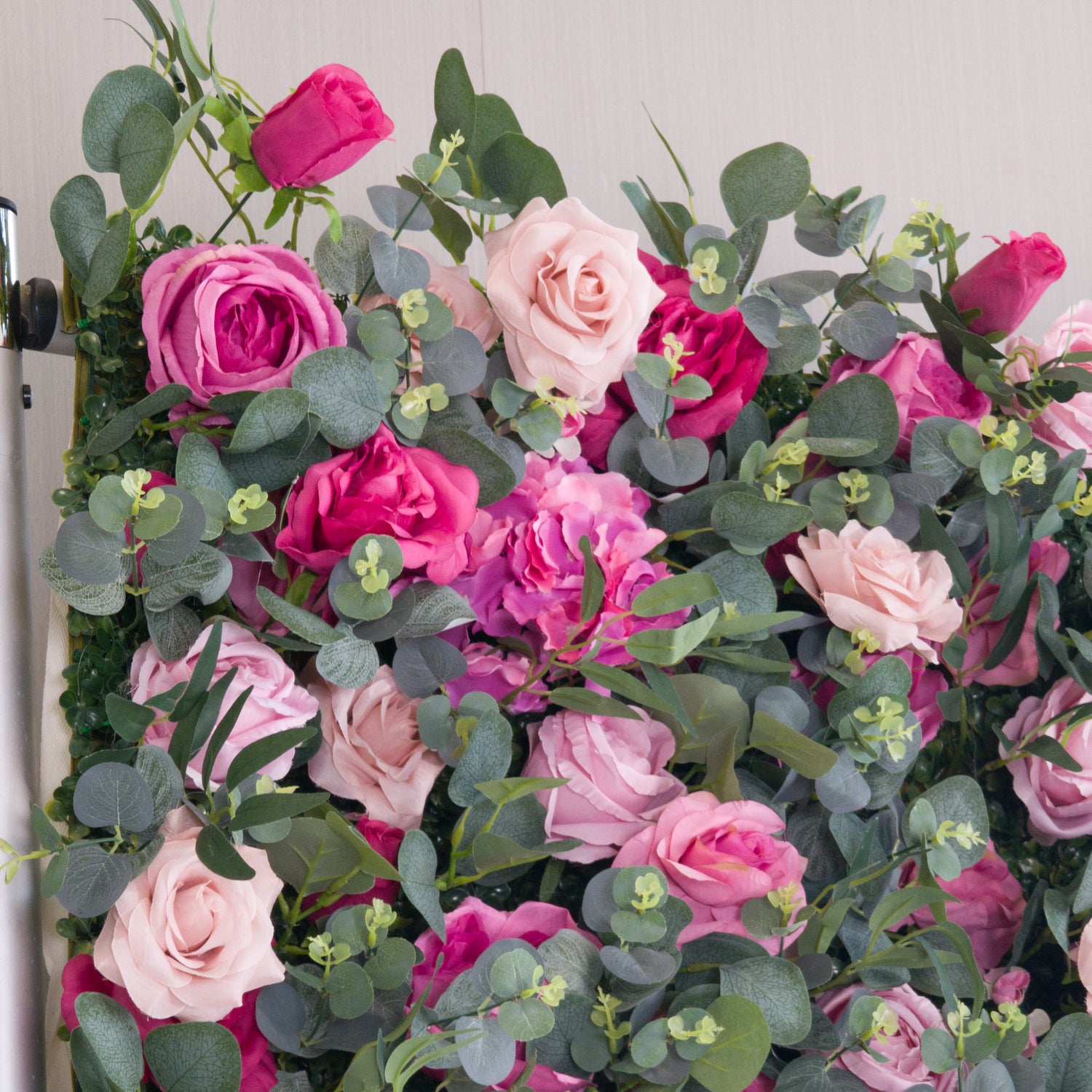 This close - up image showcases a dense arrangement of artificial flowers in various shades of pink, from light to deep hues, along with some purple blooms. Interspersed among the flowers are green eucalyptus leaves and small green buds, creating a lush and vibrant display. The harmonious blend of colors and textures gives a sense of natural beauty and elegance, making it suitable for decorative purposes in events or as an attractive interior backdrop.
