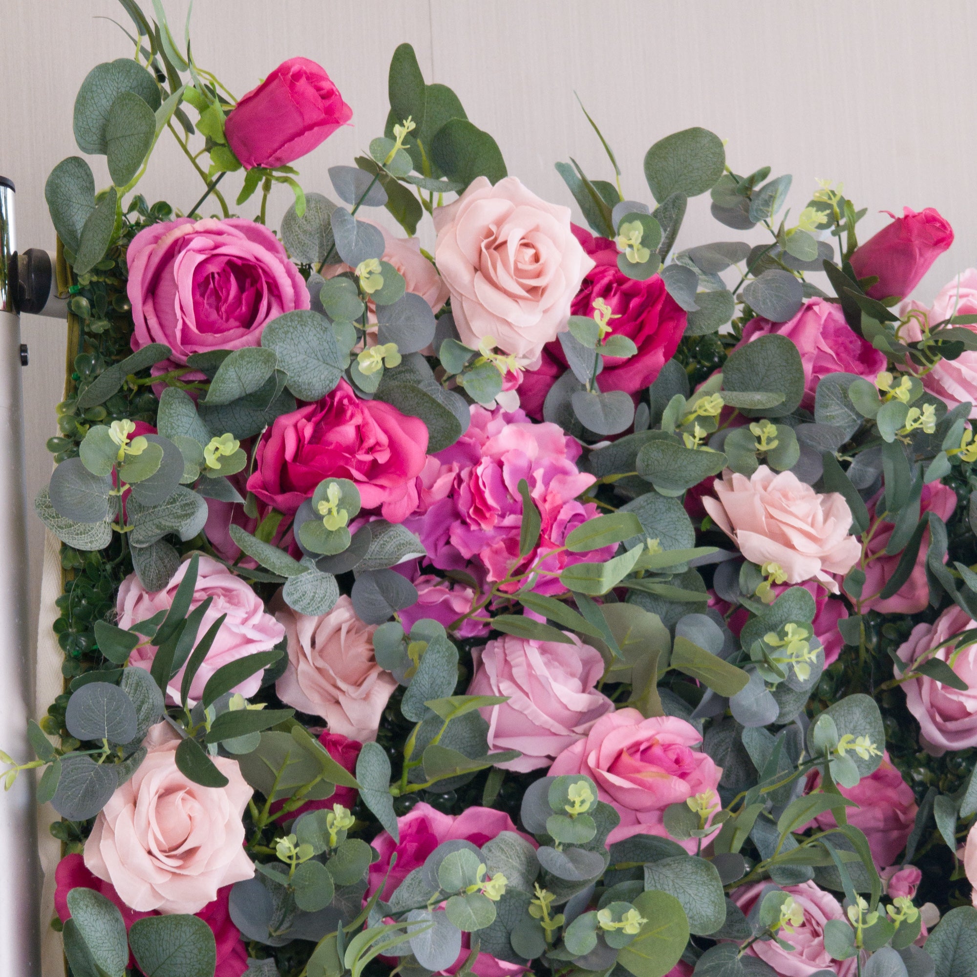 This close - up image showcases a dense arrangement of artificial flowers in various shades of pink, from light to deep hues, along with some purple blooms. Interspersed among the flowers are green eucalyptus leaves and small green buds, creating a lush and vibrant display. The harmonious blend of colors and textures gives a sense of natural beauty and elegance, making it suitable for decorative purposes in events or as an attractive interior backdrop.