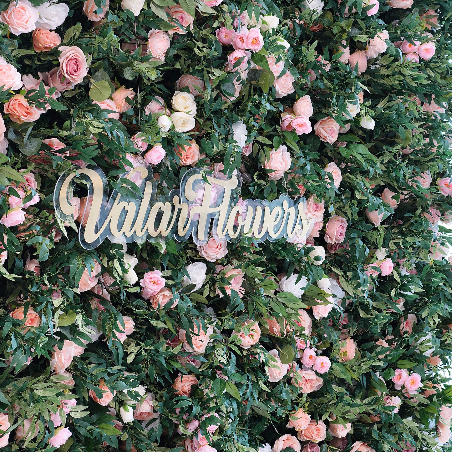This photo showcases a dense floral backdrop filled with pink and white roses interspersed among lush green foliage. The text "ValarFlowers" in elegant golden lettering stands out prominently. Ideal for events like wedding ceremonies or a "Romantic Floral Extravaganza", it creates a dreamy and sophisticated atmosphere, making it a perfect decorative centerpiece for refined and joyous occasions. 