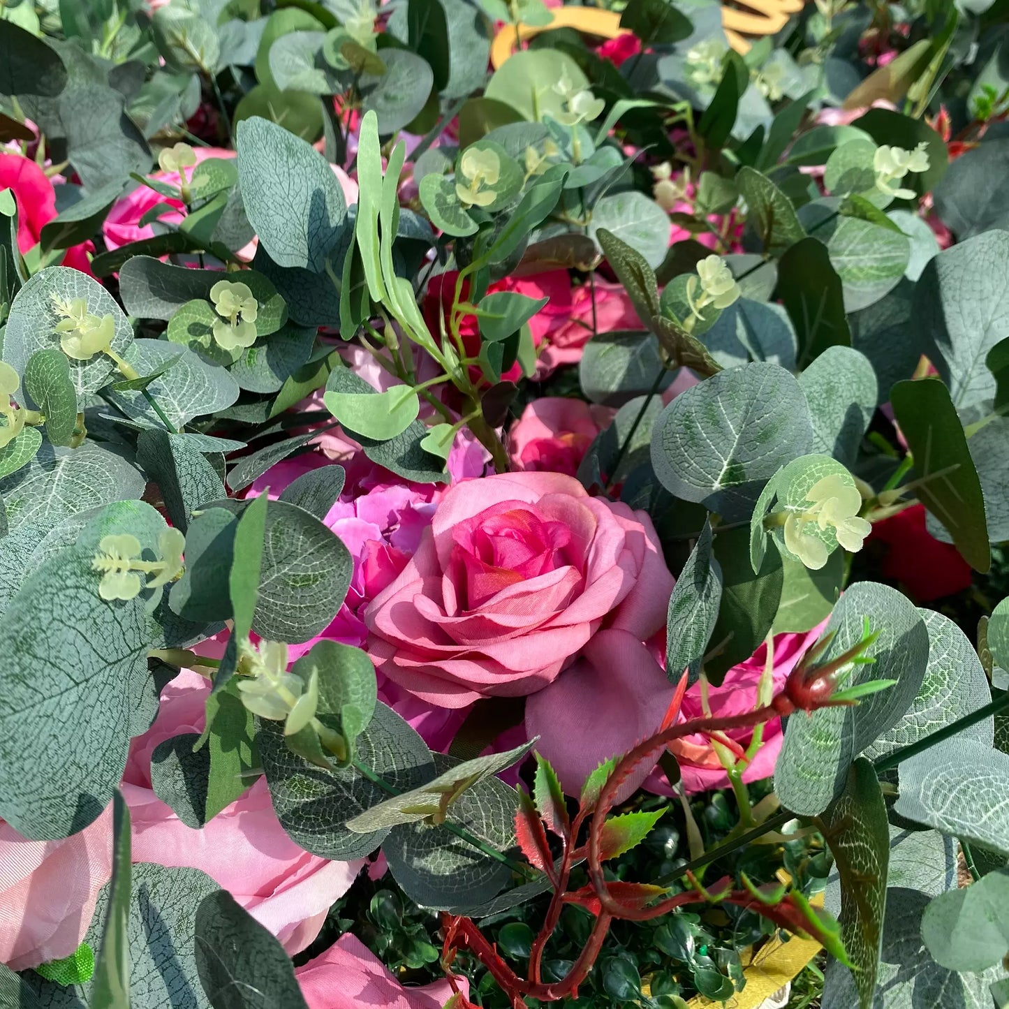 This close - up image showcases a dense arrangement of artificial flowers and foliage. At the center, there's a prominent pink rose with soft, layered petals. Surrounding it are other pink blooms, along with various green leaves, including eucalyptus - like ones with distinct veining. The harmonious blend of colors and textures creates a lush, vibrant display, ideal for decorative purposes in events or as an attractive floral arrangement.