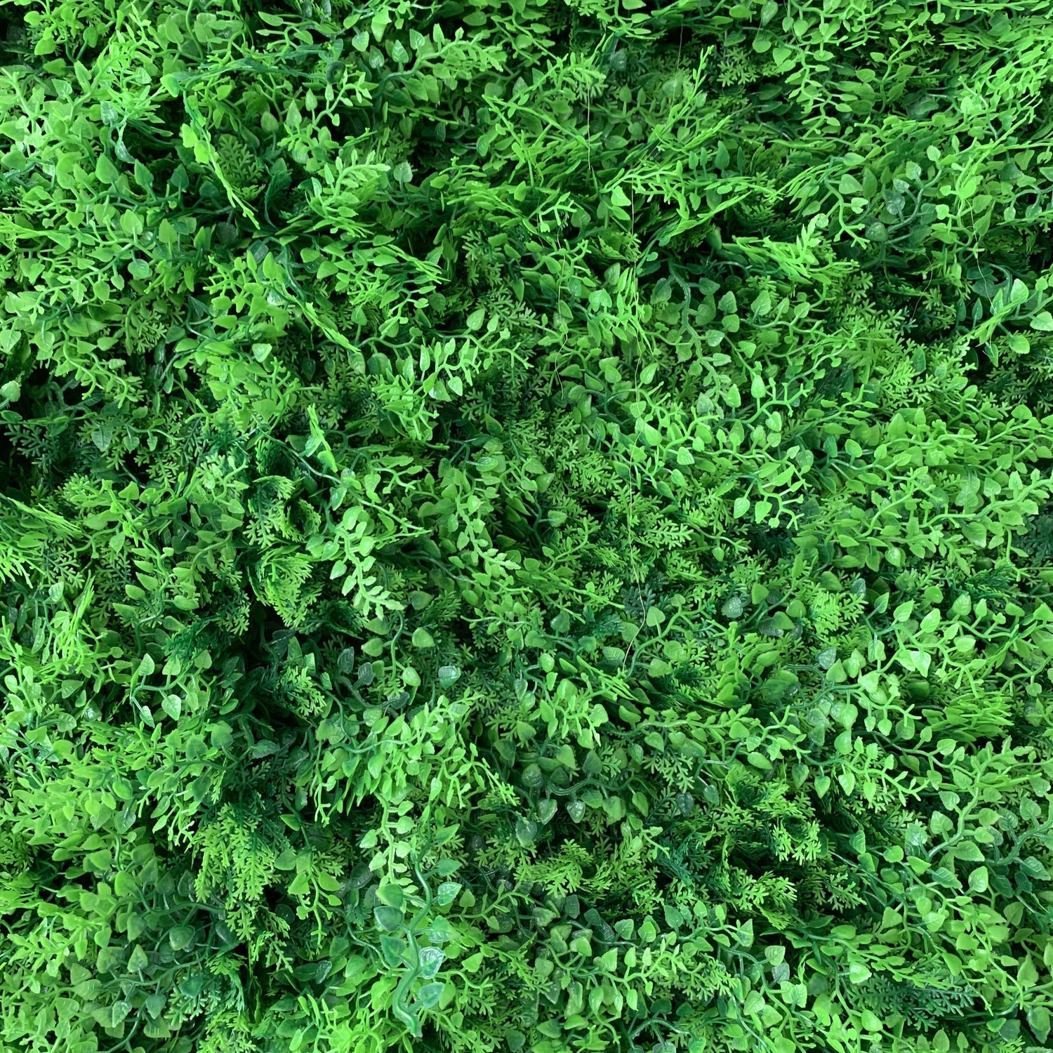 This image showcases a dense, lush expanse of artificial greenery. It features a rich variety of small, textured green leaves and foliage in different shades of green, creating a vibrant, multi-dimensional display. The intricate details and varied plant shapes give it a highly realistic, natural appearance, ideal for use as a backdrop or decor element to bring an organic, refreshing, and serene atmosphere to spaces or events.