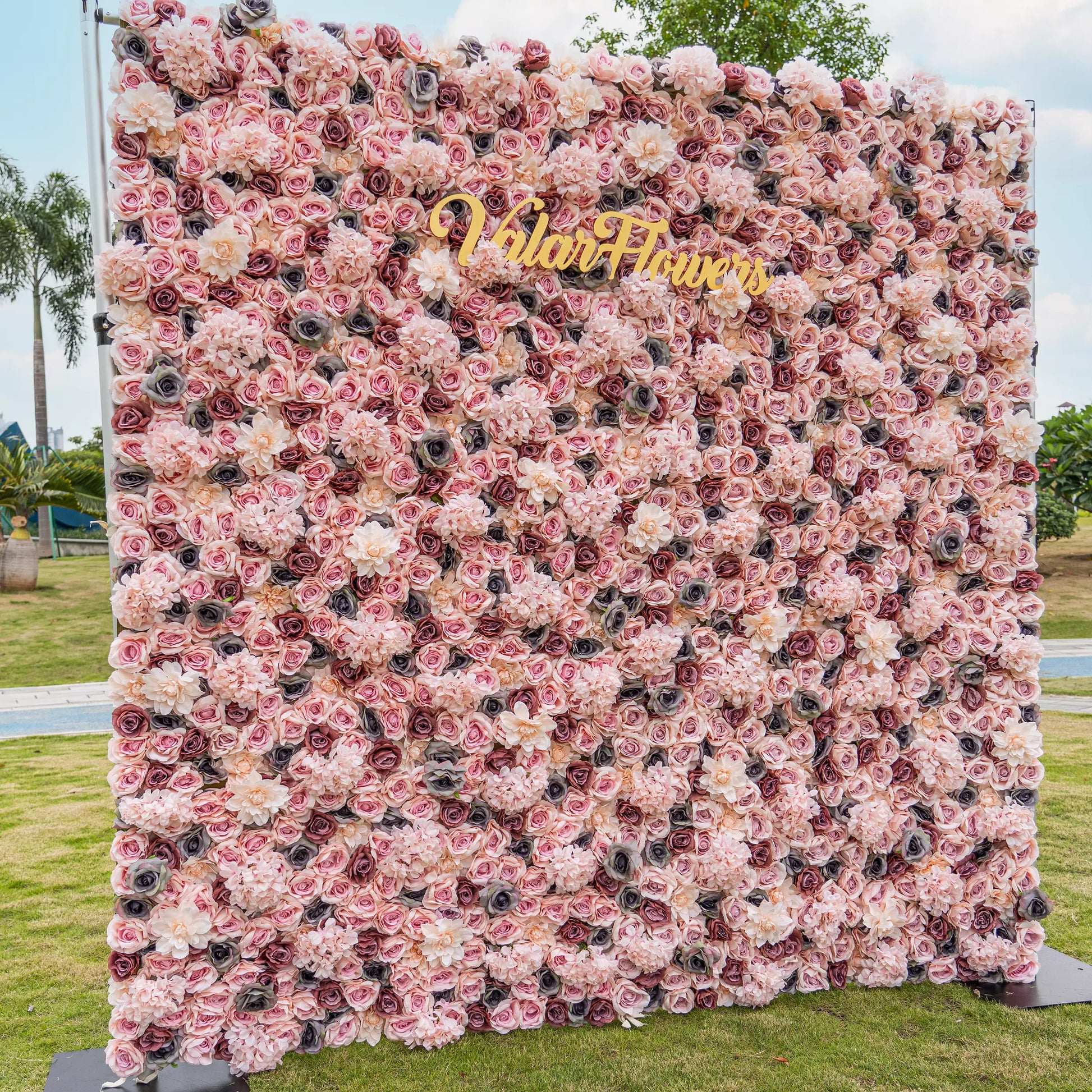 Blush Blossom Tapestry: An exquisite floral backdrop brimming with layers of soft pink and creamy white roses. Amidst the gentle petals, the golden "VlairFlowers" inscription gleams, set against a scenic city park. An embodiment of romance and elegance in nature's embrace.