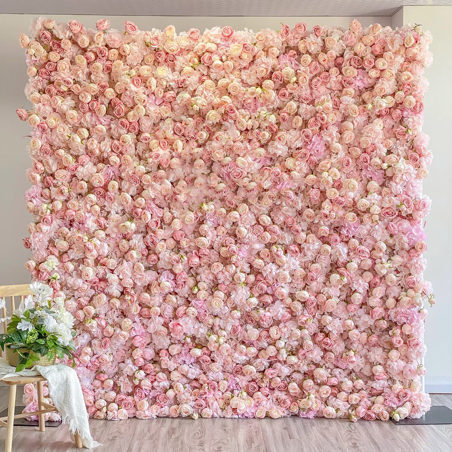 A 2.4m by 2.4m, square flower wall covered with an abundance of light pink roses. The dense arrangement of blooms creates a soft, romantic backdrop, complemented by a small bouquet on a chair beside it.
